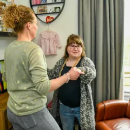 Begeleider en cliënte met verstandelijke beperking dansen in de woonkamer