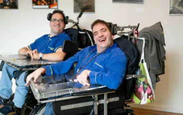 Twee lachende mannen in hun electrische rolstoelen.