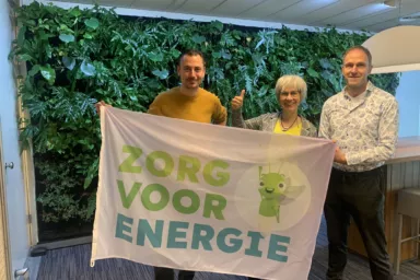 3 collega's van duurzaam ondernemen houden een campagnevlag vast met de tekst 'zorg voor energie'.