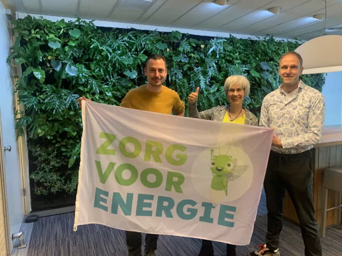 3 collega's van duurzaam ondernemen houden een campagnevlag vast met de tekst 'zorg voor energie'.